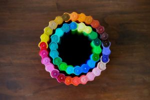 Different colour markers connected together in circles. The image is photographed from above so only the tops of the lids are visible. The table they're on is wood. It looks like two rainbow circles, one inside the other.